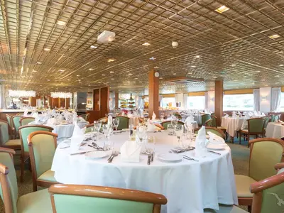 Das helle Restaurant an Bord der MS Magellan ist mit elegant gedeckten Tischen und mintgrünen Stühlen ausgestattet. Große Fenster lassen Tageslicht herein. Eine einladende Atmosphäre für Mahlzeiten.