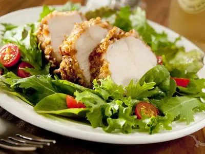 Nahaufnahme eines appetitlichen Tellers mit frisch zubereitetem Salat und geschnittenem, paniertem Hähnchenbrustfilet, garniert mit Kirschtomaten, serviert an Bord der MS Magellan.