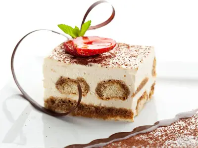Ein quadratisches Stück Tiramisu mit Kakaopulver, garniert mit einer halbierten Erdbeere, Minze und Schokospäne, serviert auf einem weißen Teller an Bord der MS Rhein Prinzessin.