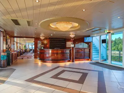 Elegante Rezeption der MS Rhein Prinzessin. Eine polierte Holztheke, großer Kronleuchter. Dahinter Schließfächer, ein Restaurant und Fenster mit Blick ins Grüne.