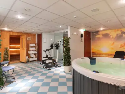 Innenansicht des Wellnessbereichs an Bord der MS Rhein Prinzessin. Ein Whirlpool mit sprudelndem Wasser, eine Holzsauna, zwei Ergometer und ein Handtuchregal sind zu sehen. Der Boden hat ein blau-weißes Rautenmuster.