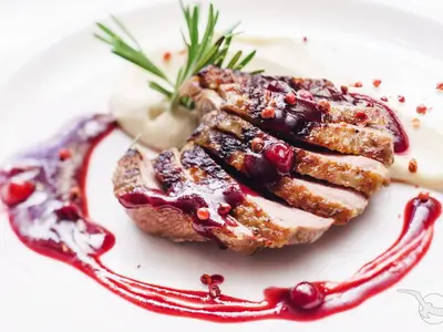 Nahaufnahme eines Gourmet-Gerichts mit Entenbrust, Beerensoße und Rosmarin, kunstvoll auf weißem Teller angerichtet. Zu sehen an Bord der MS Rhein Prinzessin.