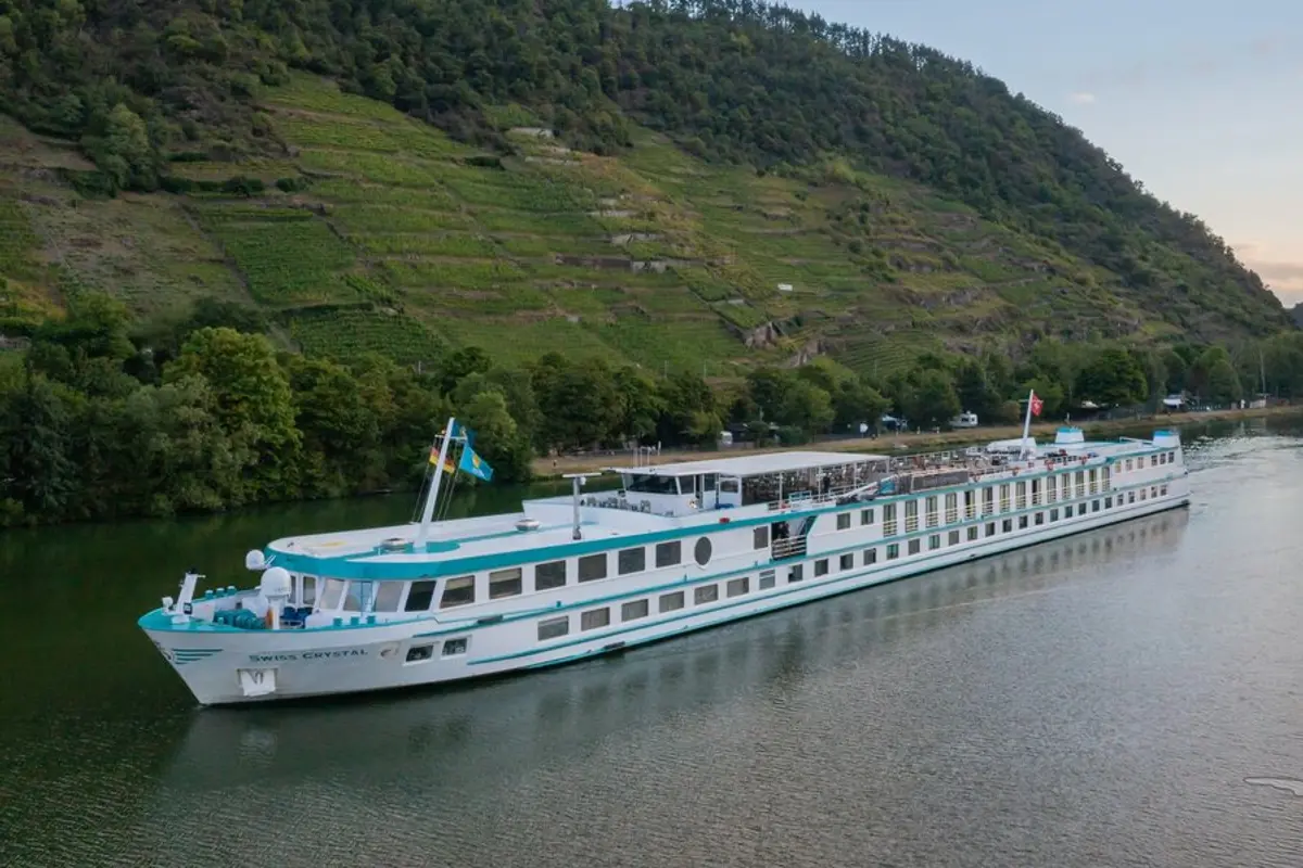 Die MS Swiss Crystal gleitet auf einem Fluss entlang, umgeben von grüner Vegetation und terrassierten Weinbergen an den Ufern. Der Himmel ist leicht bewölkt.