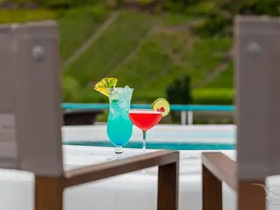 Zwei erfrischende Cocktails, ein blauer mit Ananas und ein roter mit Limette, stehen am Pool der MS Swiss Crystal. Im Hintergrund sind grüne, terrassierte Hänge sichtbar.