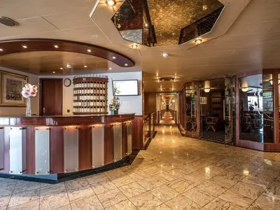 Blick auf die Rezeption und eine angrenzende Lounge der MS Swiss Crystal. Ein geschwungener Holz-Tresen mit Beleuchtung steht im Vordergrund, dahinter ein Schlüsselfachregal. Ein langer Gang führt in die Tiefe.