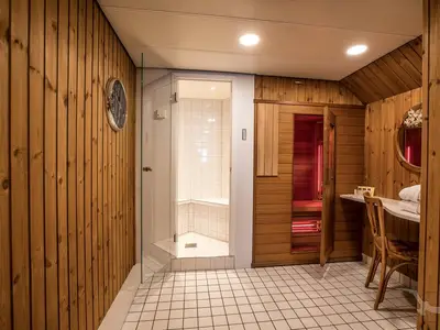 Blick in einen privaten Wellnessbereich an Bord der MS Swiss Crystal. Zu sehen sind eine gläserne Dusche, eine Holzkabine mit geöffneter Saunatür und roten Lichtern, sowie ein Waschtisch mit Spiegel.