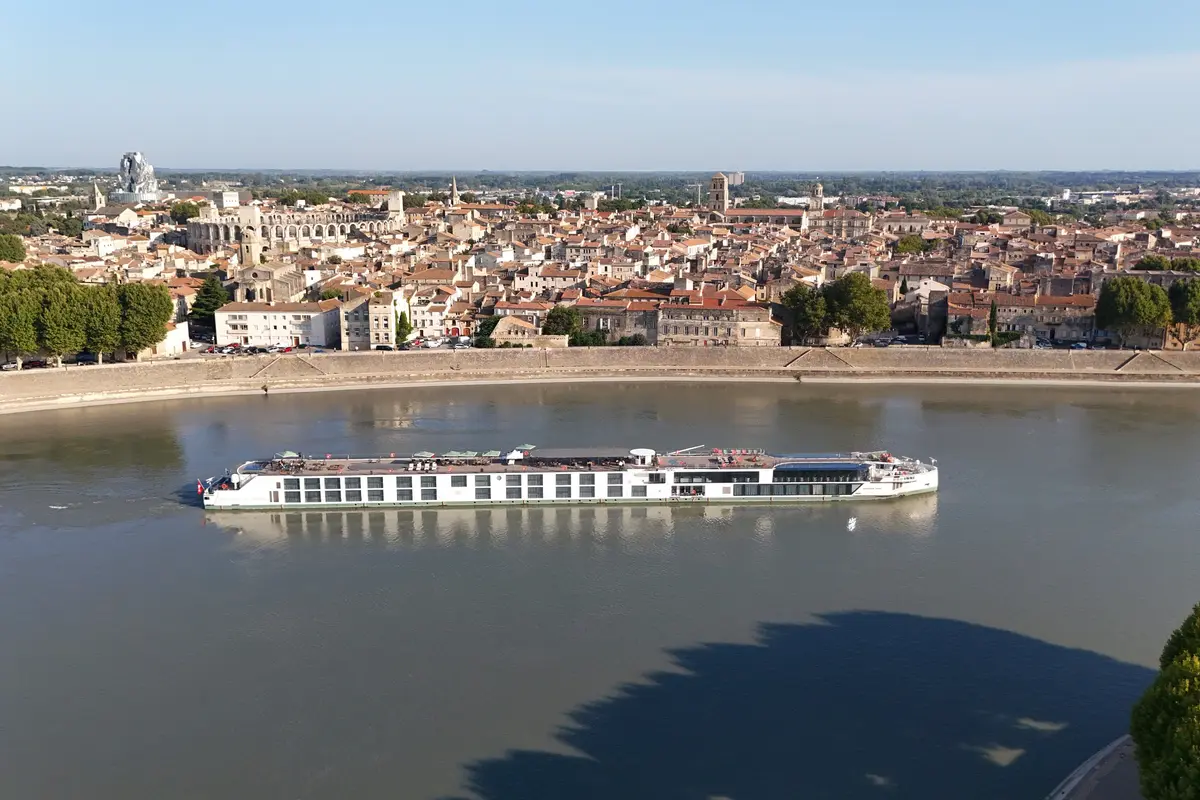 Die Riverside Debussy auf einem Fluss vor einer historischen Stadt mit vielen Dächern und einem modernen Turm unter klarem Himmel. Blick aus der Vogelperspektive.