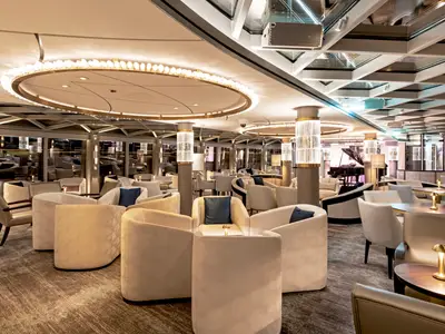 Der elegante Palm Court an Bord der Riverside Debussy zeigt helle Sessel, runde Tische, beleuchtete Säulen und eine Glasdecke. Ein Flügel im Hintergrund deutet auf Live-Musik hin.
