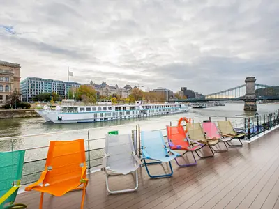 Blick vom Sonnendeck der Riverside Debussy mit bunten Liegestühlen auf die Donau. Im Hintergrund sind die Stadt Budapest, die Kettenbrücke und ein weiteres Flussschiff zu sehen.