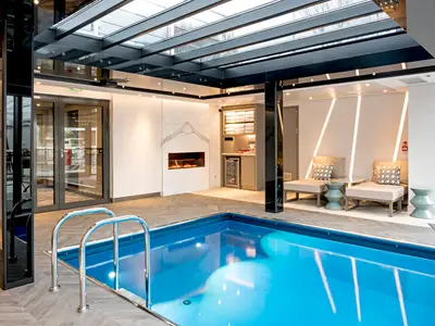 Der elegante Innenpool an Bord der Riverside Debussy. Der blaue Pool wird von modernen Lounge-Sesseln, einem Kamin und einer Bar flankiert. Ein Glasdach erhellt den stilvollen Raum.