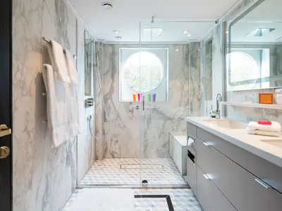 Modernes Badezimmer einer Suite an Bord der Riverside Debussy. Es zeigt einen Waschtisch, eine geräumige Dusche mit Glaswand und ein markantes Rundfenster.