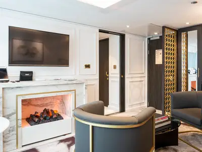 Elegante Suite an Bord der Riverside Debussy. Im Bild: Ein Kamin mit TV, moderne Sessel, weisse Wandpaneele und goldene Akzente. Luxuriöses Interieur.