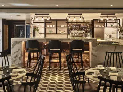 Eine modern eingerichtete Bar-Lounge an Bord der Riverside Mozart mit Marmortheke, schwarzen Barhockern und kleinen Tischen, gedeckt mit Geschirr. Warme Beleuchtung und geometrischer Fussboden.