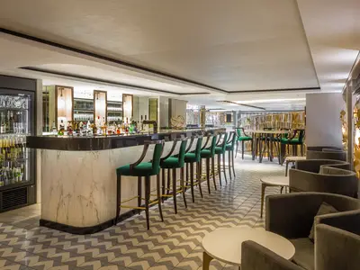 Die elegante Cove Bar an Bord der Riverside Mozart zeigt eine Marmortheke, Flaschen, grüne Samtstühle und eine gemusterte Fliese. Im Hintergrund loungeähnliche Sitzbereiche und goldene Wandkunst.