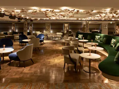 Elegante Bar-Lounge an Bord der Riverside Mozart mit bequemen Sitzbereichen, geschwungenem grünem Sofa und Flügel. Kunstvolle Blatt-Deckenbeleuchtung.