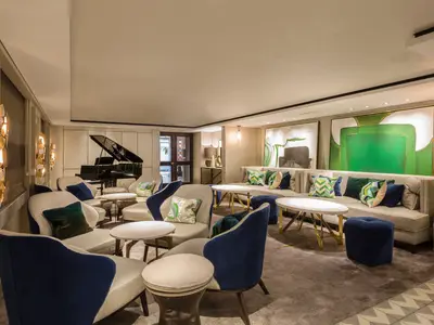 Eine stilvolle Lounge an Bord der Riverside Mozart, ausgestattet mit bequemen Sesseln, Sofas und einem schwarzen Grand Piano. Die Einrichtung ist modern, ergänzt durch grüne und blaue Kissen sowie Wandkunst.