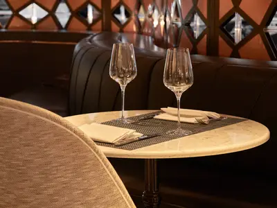 Ein elegant gedeckter runder Marmortisch für zwei Personen mit Weingläsern, Besteck und Servietten im Restaurant der Riverside Mozart. Dunkle, gepolsterte Sitzbänke im Hintergrund.