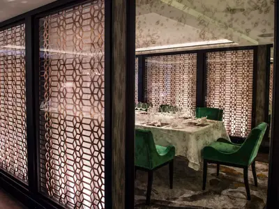 Ein luxuriöser privater Speisesaal an Bord der Riverside Mozart mit einem elegant gedeckten Tisch und grünen Samtstühlen. Die Wände sind mit dekorativen, beleuchteten Metallgittern im Wabenmuster verziert.