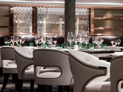 Ein stilvolles Restaurant an Bord der Riverside Mozart, detailreich gedeckt mit weissen Tischdecken, klaren Weingläsern und markanten grünen Wassergläsern. Elegante Stühle säumen die Tische in einer luxuriösen Innenumgebung.