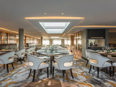 Das helle und moderne Waterside Restaurant an Bord der Riverside Mozart zeigt elegant gedeckte Tische mit weissen Ledersesseln und grünen Akzenten. Grosse Oberlichter und Fensterfronten sorgen für viel Tageslicht, ergänzt durch indirekte Beleuchtung. Der Raum ist luxuriös eingerichtet mit Holz- und Glaselementen.