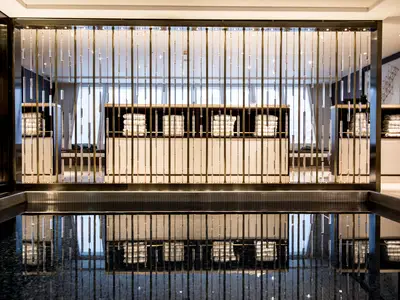 Blick auf den stilvollen Innenpool-Bereich an Bord der Riverside Mozart. Eine transparente Trennwand mit vertikalen Stäben trennt den Pool vom Hintergrund. Dahinter sind Ablagen mit gestapelten weißen Handtüchern zu sehen, die sich im dunklen Wasser spiegeln.