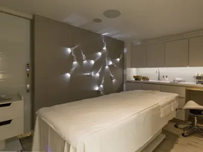 Moderner Spa-Behandlungsraum an Bord der Riverside Mozart. Ein weisses Massagebett, eine Wand mit indirekter Beleuchtung und ein Waschtisch mit Pflegeprodukten.