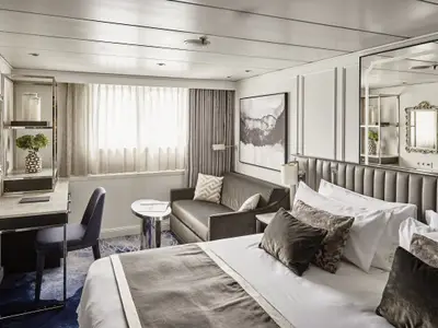 Eine luxuriöse Harmony Suite an Bord der Riverside Mozart mit grossem Doppelbett, samtig gepolstertem Kopfteil und einem gemütlichen Sofa. Ein Schreibtisch und Fenster sind ebenfalls zu sehen.