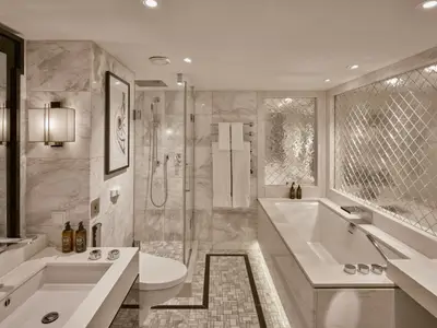 Elegantes Badezimmer einer Suite an Bord der Riverside Mozart. Es zeigt Badewanne, Dusche, Waschtisch mit Spiegel und luxuriöse Marmoroberflächen in warmem Licht.