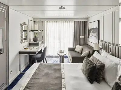 Geräumige Suite an Bord der Riverside Mozart. Mit großem Bett, Sofa, Schreibtisch und Balkontür. Elegante, moderne Einrichtung in Grau- und Weißtönen.