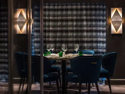 Elegantes Restaurant auf der Riverside Ravel. Gedeckter Tisch mit Weingläsern, grünen Bechern und blauen Samtstühlen. Moderne Tapete und Wandleuchten.