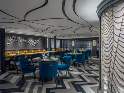 Elegantes Restaurant an Bord der Riverside Ravel. Der Innenraum zeigt blaue Samtstühle, orangefarbene Bänke, modern gedeckte Tische und eine kunstvolle, wellenförmige Decke.