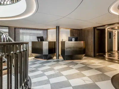 Eine elegante Rezeption an Bord der Riverside Ravel. Zwei dunkle, moderne Empfangstheken stehen auf einem schwarz-weiss karierten Boden, links eine geschwungene Treppe mit Metallgeländer. Die Decke ist hell und beleuchtet.