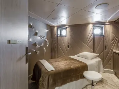 Luxuriöser Spa-Behandlungsraum an Bord der Riverside Ravel. Ein Behandlungsbett, elegante Wände mit geometrischen Mustern und indirekter Beleuchtung. Ein 'VACANT'-Schild an der Tür.