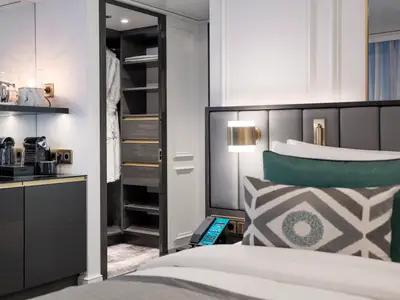 Blick in eine elegante Suite an Bord der Riverside Ravel. Zu sehen sind ein komfortables Bett mit Zierkissen, eine Kaffeemaschine und ein offener Kleiderschrank mit Bademantel. Die moderne Einrichtung lädt zum Entspannen ein.