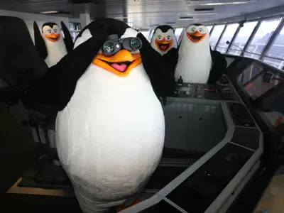 Vier Pinguin-Maskottchen auf der Kommandobrücke der Allure of the Seas. Einer hält ein Fernglas. Drei weitere stehen hinter den Steuerkonsolen des Schiffes.