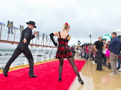 Ein Tanzpaar tanzt auf einem roten Teppich an Deck der Allure of the Seas. Pressevertreter filmen. Im Hintergrund 'Puss in Boots'-Schilder und das Meer.