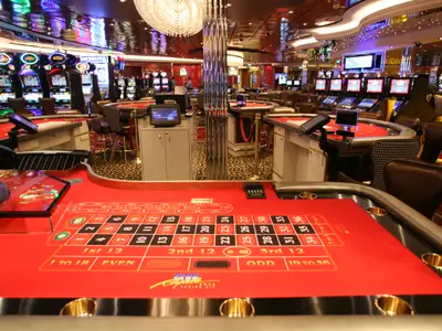 Das Casino der Allure of the Seas. Roter Roulettetisch im Vordergrund, dahinter viele Spielautomaten und Casinotische. Ein hell beleuchteter Raum an Bord.