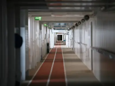 Blick in einen langen Gang an Bord der Allure of the Seas. Ein roter Laufsteg mit weißen Linien führt in die Tiefe. Schilder mit 'WRONG WAY' sind sichtbar.