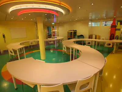 Kunst- und Bastelraum der Allure of the Seas mit geschwungenen Tischen, bunten Böden und großen Buntstiften. Ein farbenfroher Ort für kreative Kinder.