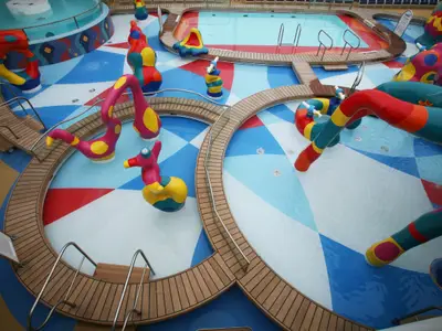 Luftaufnahme des bunten Kinder-Wasserparks an Bord der Allure of the Seas von Royal Caribbean International mit Wasserspielfiguren, flachen Pools und Holzdecks.