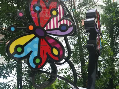 Nahaufnahme einer farbenfrohen Schmetterlings-Skulptur mit geometrischen Mustern im Stil von Romero Britto, an Bord der Allure of the Seas. Die lebhafte Kunstinstallation ist umgeben von üppigem Grün.