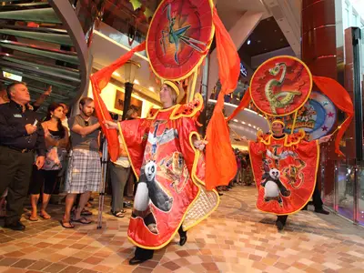 Zwei in Kung Fu Panda-Kostümen gekleidete Darsteller paradieren auf der Royal Promenade der Allure of the Seas, beobachtet von Zuschauern.