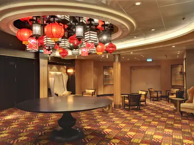 Luxuriöse Lounge im Inneren der Allure of the Seas. Eine große Deckenleuchte mit roten Laternen ist zentral. Bunter Teppich, ovaler Tisch und diverse Sessel gestalten den Raum.
