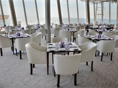 Ein heller Restaurantbereich der Allure of the Seas mit zahlreichen gedeckten Tischen und weißen Stühlen. Große Panoramafenster bieten einen weiten Blick auf das offene Meer.