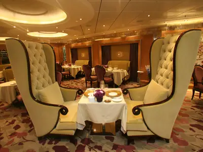 Das Restaurant der Allure of the Seas zeigt luxuriöse Ohrensessel und gedeckte Tische in einem warmen, eleganten Ambiente.