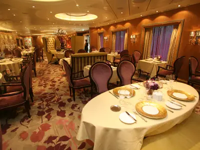 Restaurant auf der Allure of the Seas: Elegante Tische mit goldenen Tellern, violette Stühle, floraler Teppich, holzgetäfelte Wände.