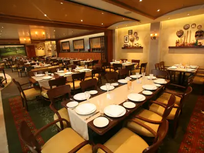 Ein elegantes Restaurant an Bord der Allure of the Seas. Gedeckte Tische, Holzstühle, warme Beleuchtung, Wanddekorationen. Einladende Atmosphäre.