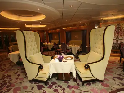 Restaurant auf der Allure of the Seas. Zwei hohe Sessel stehen an einem gedeckten Tisch. Im Hintergrund sind weitere Tische, Booths und Wandkunst sichtbar.