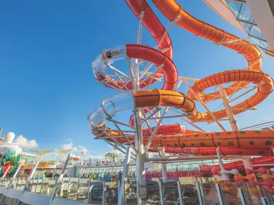 Bunte Wasserrutschen der Allure of the Seas. Rote, orange, transparente Röhren mit Badegästen unter blauem Himmel. Teile des Decks im Hintergrund.