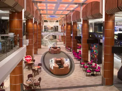 Atrium der Anthem of the Seas: Ein modernes Interieur mit Holzsäulen, hellen Sitzbereichen, zentralen Kiosken und einer großen Wendeltreppe.
